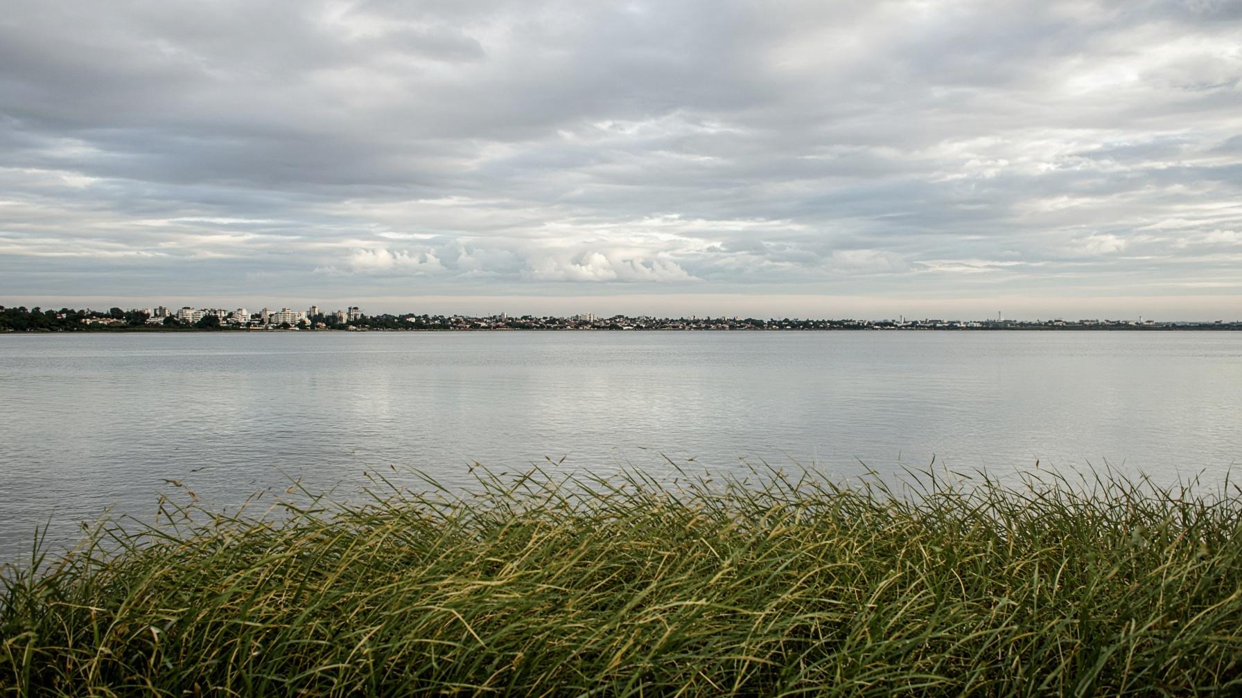 Lagoa larga sob céu nublado, com a cidade baixa no horizonte.